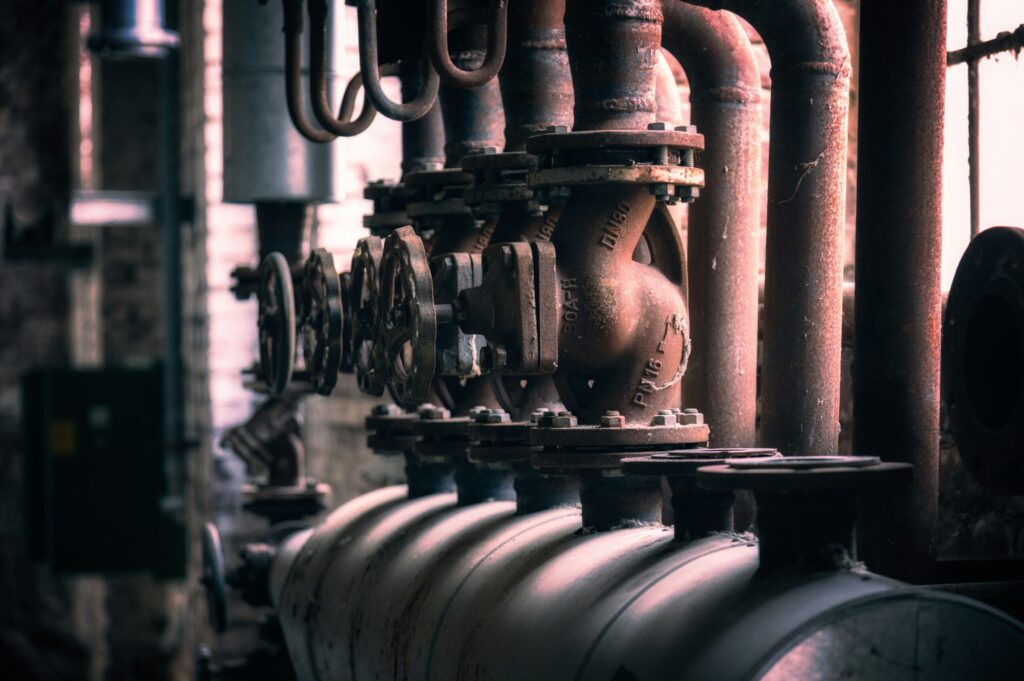 Vintage water heater pipes with rusty valves and wheel handles in mechanical room - Crest Plumbing