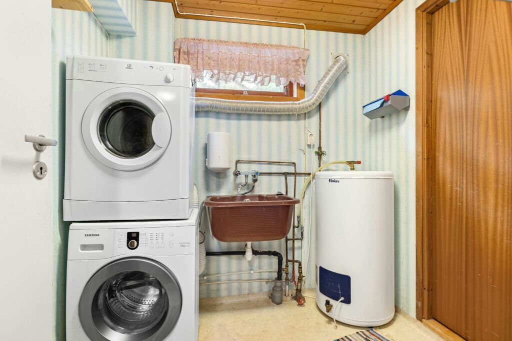Home utility room with a stacked washing machine and dryer, a slop sink, and a residential boiler or hot water tank - Crest Plumbing